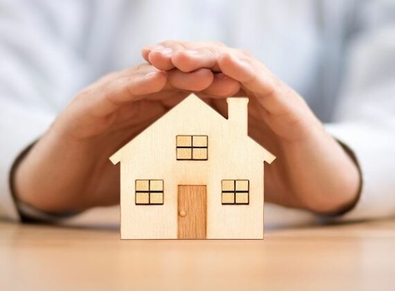 Hands covering wood house cutout representing home insurance coverage in Haskins, OH